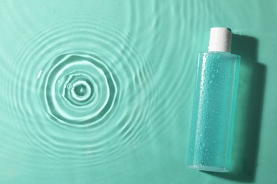 Photo of Bottle of micellar water in liquid on turquoise background, top view. Space for text