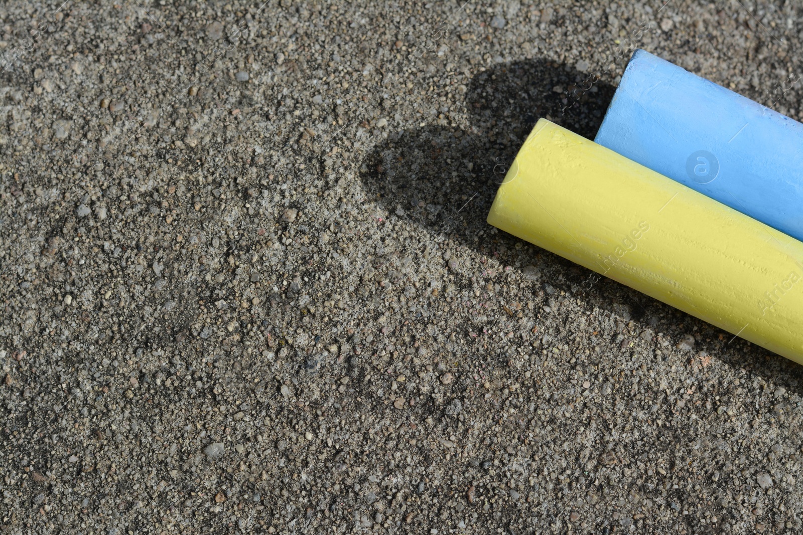 Photo of Yellow and light blue chalk sticks on asphalt, flat lay. Space for text