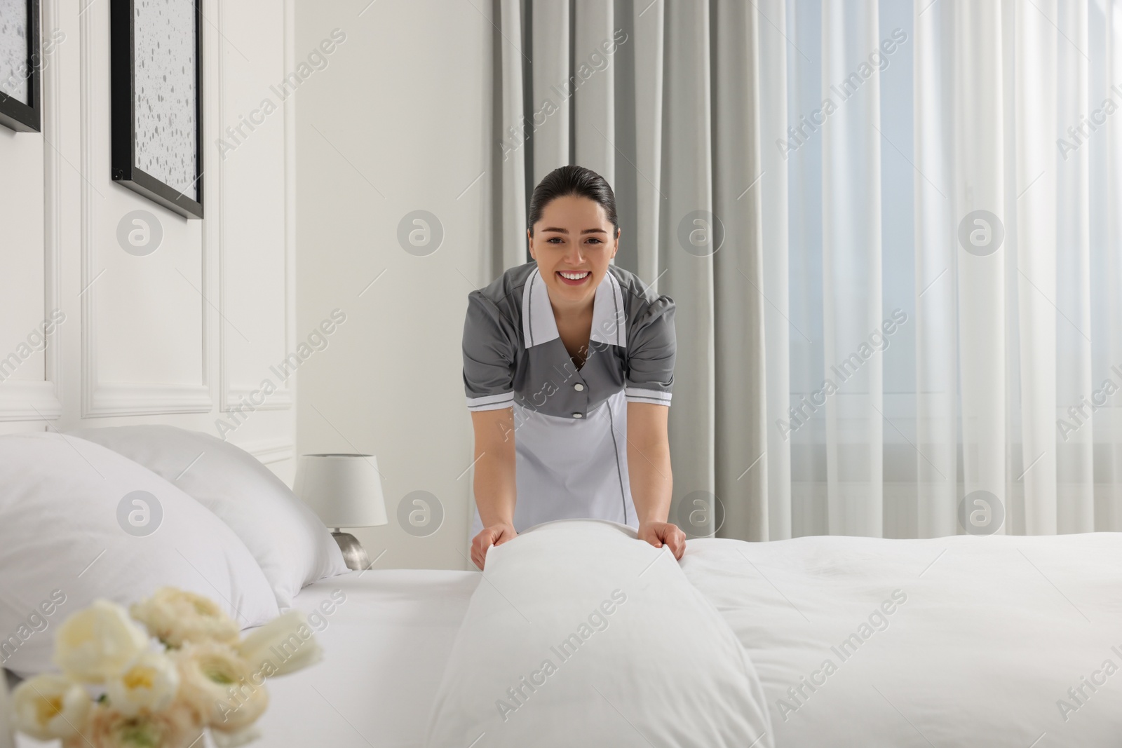 Photo of Young maid making bed in hotel room