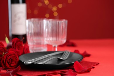Place setting with roses for romantic dinner on red table, closeup. Space for text