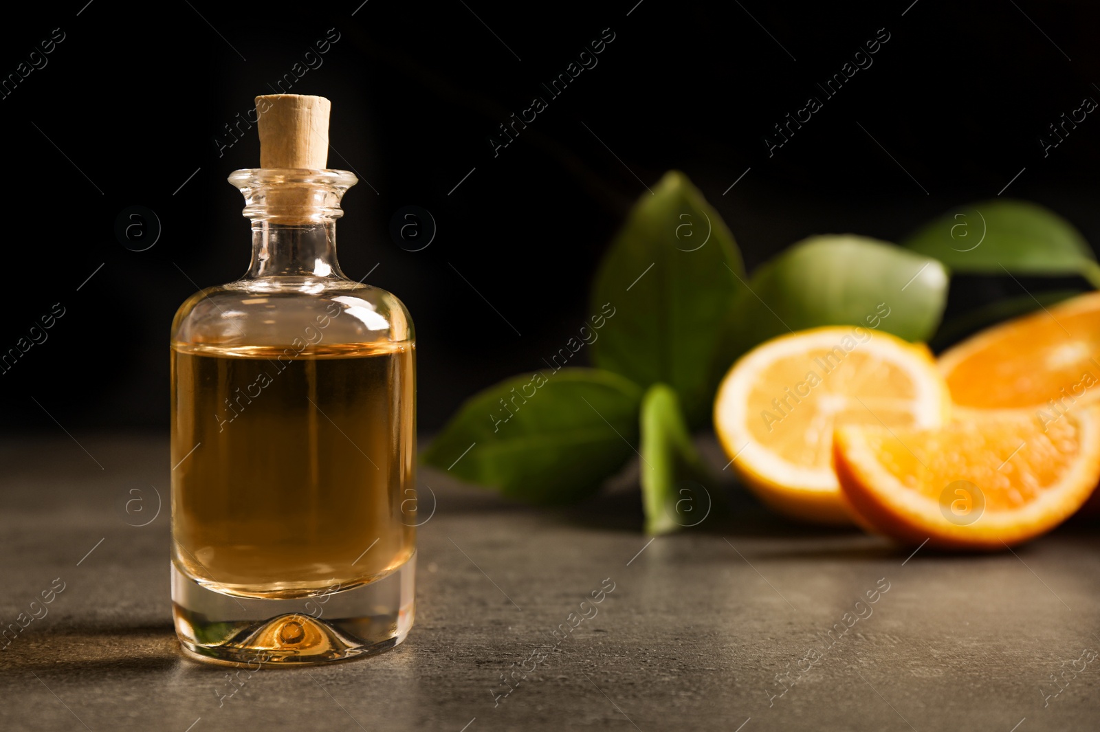 Photo of Bottle of essential oil and citrus fruits on grey table. Space for text