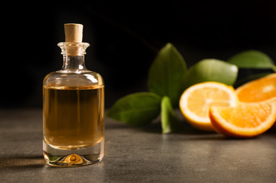 Photo of Bottle of essential oil and citrus fruits on grey table. Space for text