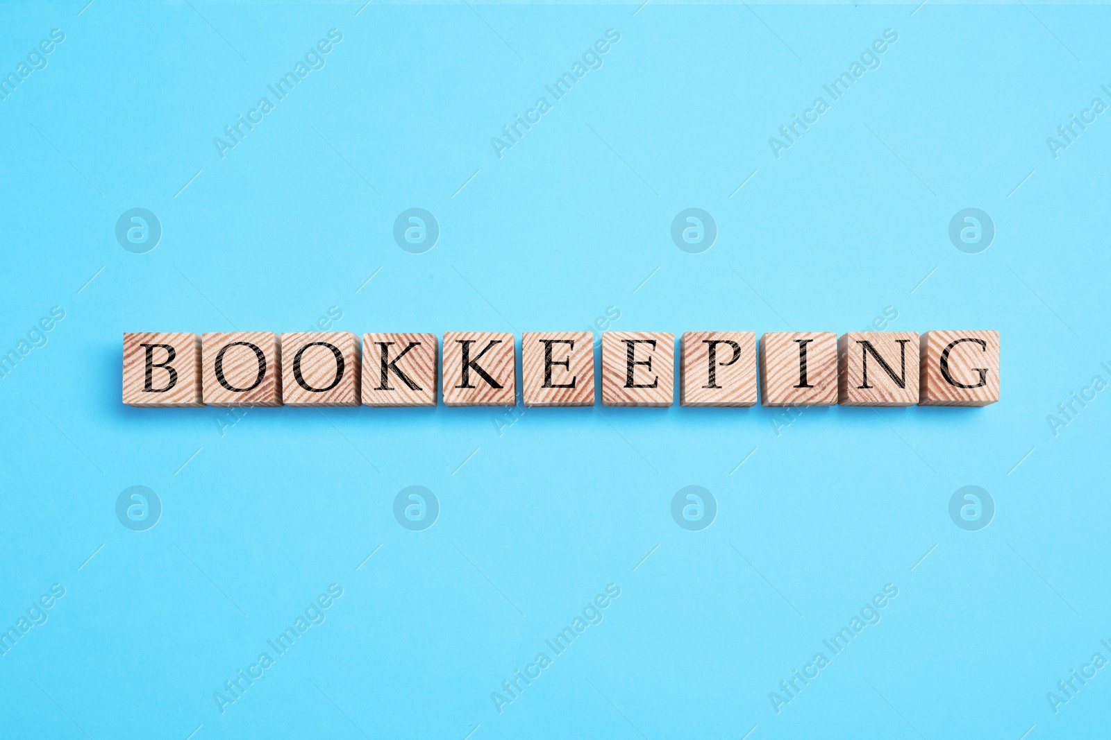 Photo of Word Bookkeeping made with wooden cubes on light blue background, top view