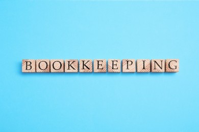 Photo of Word Bookkeeping made with wooden cubes on light blue background, top view