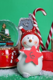 Decorative snowman with paper tag, gift box and festive decor on green background. December, 6 - Saint Nicholas Day