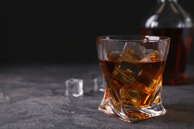 Golden whiskey in glass with ice cubes on table. Space for text