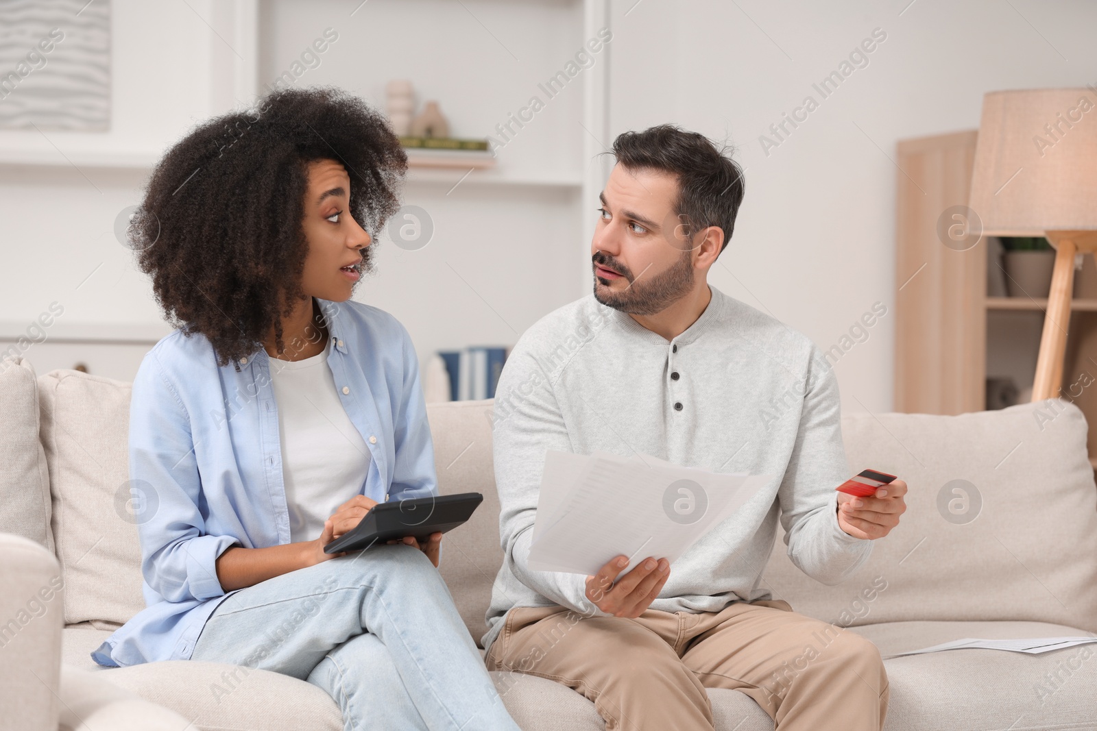 Photo of Confused couple with debt notifications, calculator and credit card planning budget at home. Financial problem