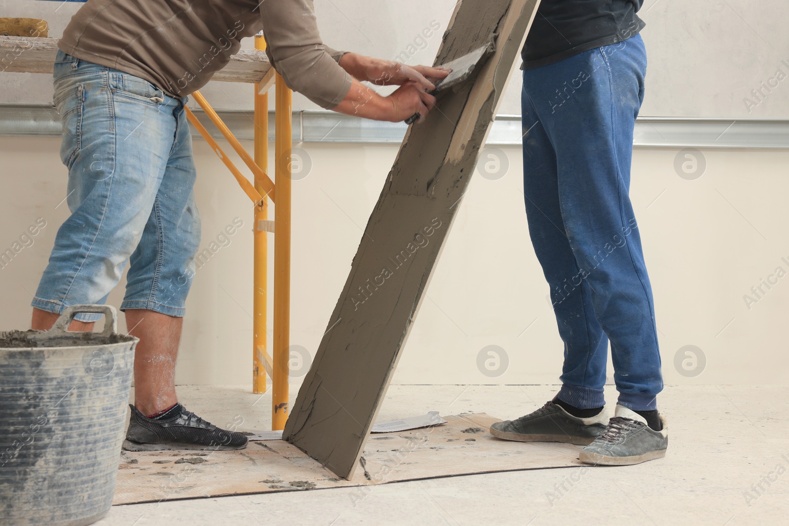 Photo of Worker spreading adhesive mix over tile with spatula, closeup