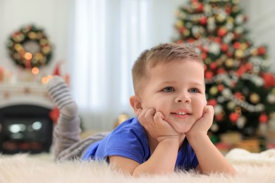 Photo of Cute little boy lying on faux fur rug in room decorated for Christmas