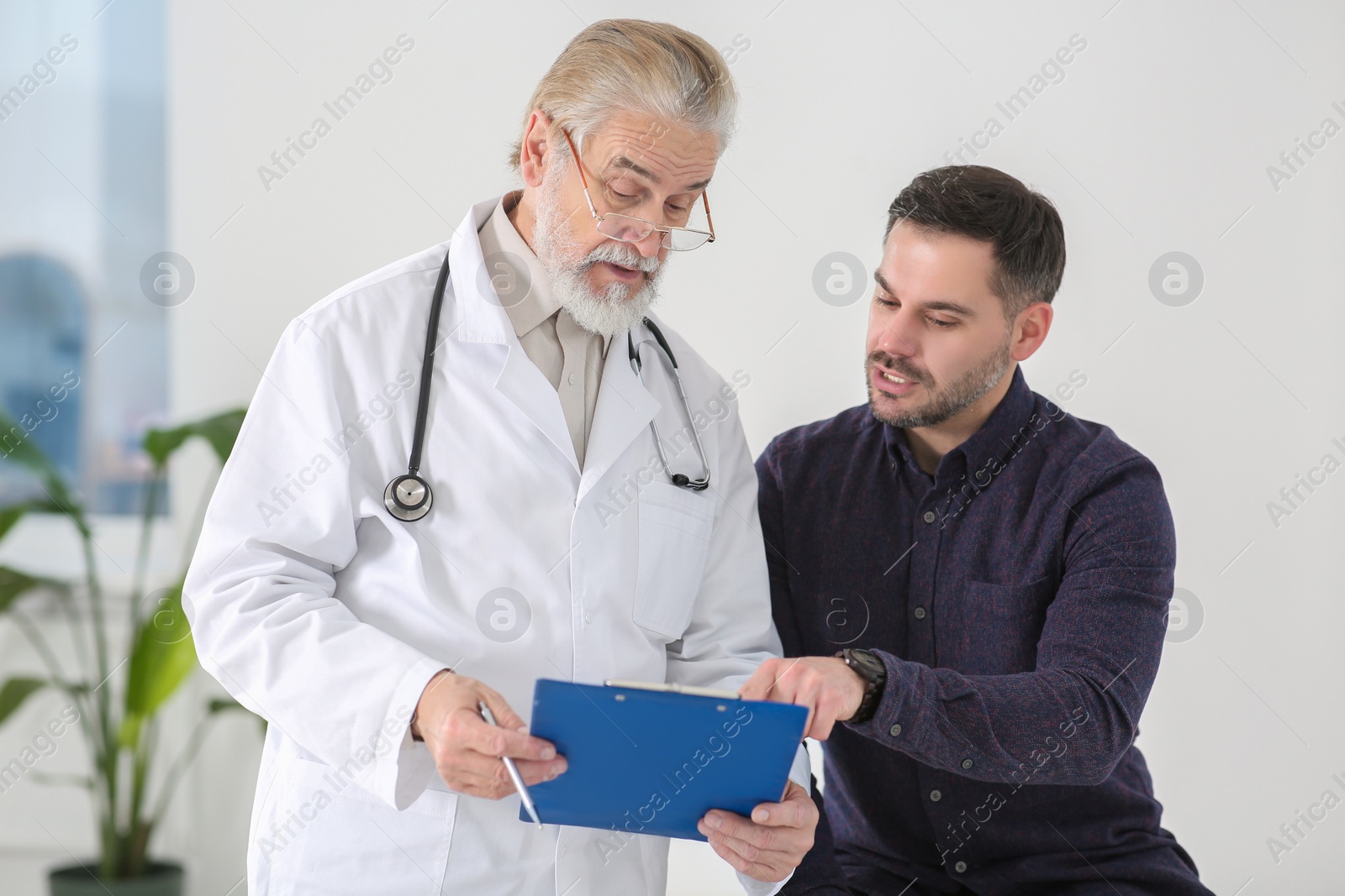 Photo of Senior doctor with clipboard consulting patient in clinic