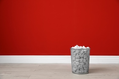 Photo of Metal bin with crumpled paper on floor against color wall. Space for text