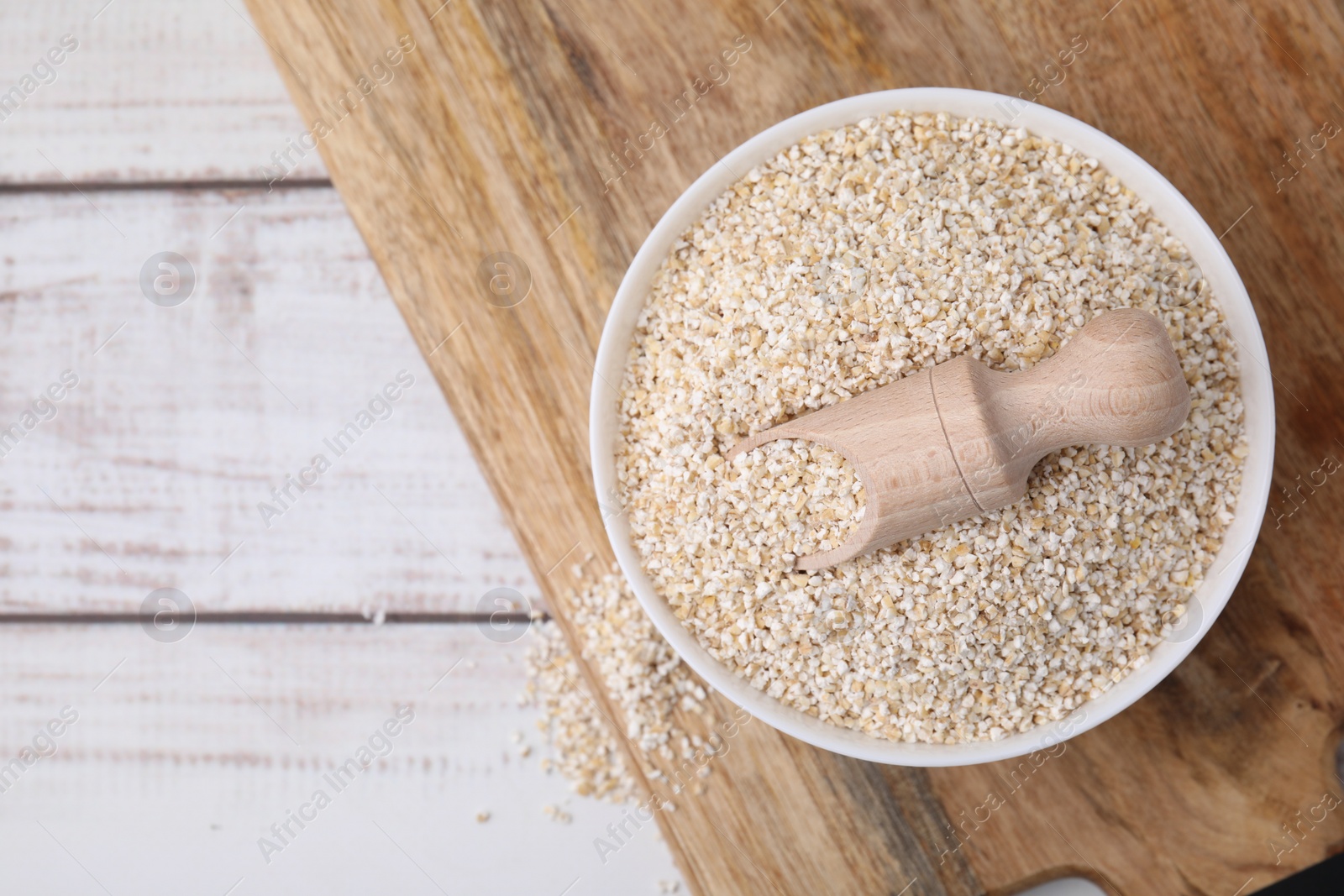 Photo of Raw barley groats and scoop in bowl on light wooden table, top view. Space for text