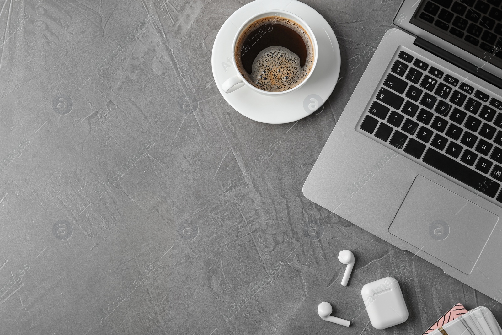 Photo of Flat lay composition with wireless earphones and laptop on grey stone table. Space for text