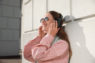 Photo of Smiling woman in headphones listening to music near building outdoors