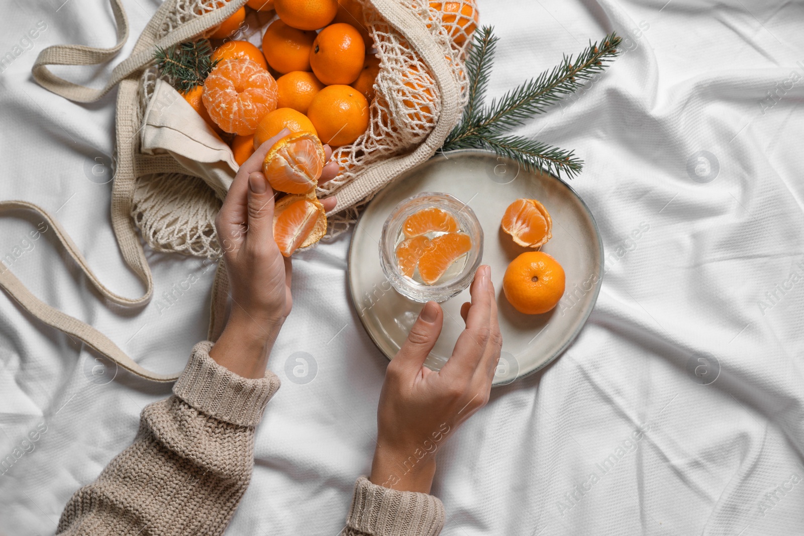 Photo of Woman with delicious ripe tangerines and glass of sparkling wine on white bedsheet, top view