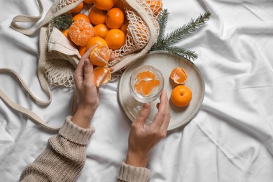 Photo of Woman with delicious ripe tangerines and glass of sparkling wine on white bedsheet, top view