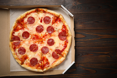 Photo of Hot delicious pepperoni pizza in cardboard box on wooden table, top view. Space for text