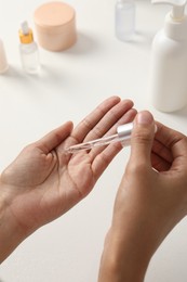 Woman applying cosmetic serum onto her hand at white table, closeup