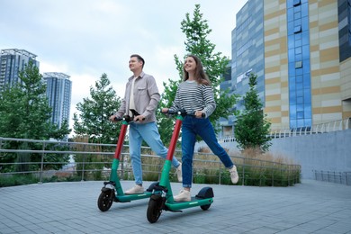 Photo of Happy couple riding modern electric kick scooters on city street