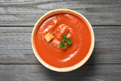 Photo of Bowl with fresh homemade tomato soup on wooden background, top view