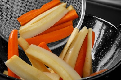 Putting cut parsnips and carrots into wok pan, closeup