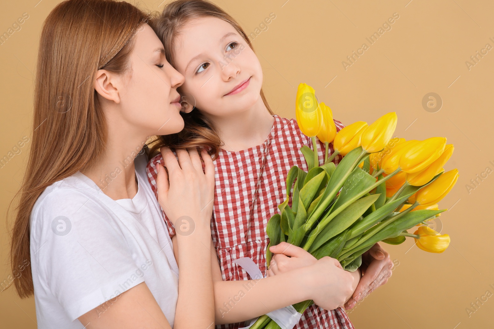 Photo of Mother and her cute daughter with bouquet of yellow tulips on beige background