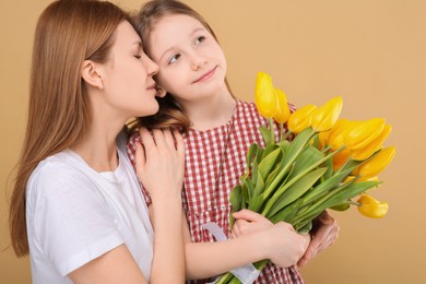 Mother and her cute daughter with bouquet of yellow tulips on beige background