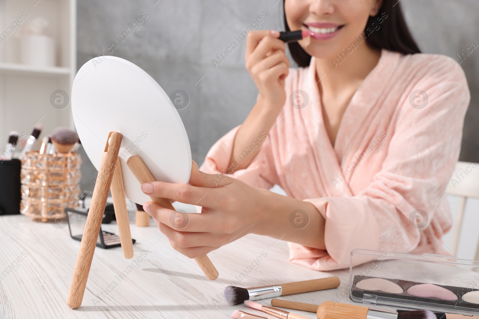 Photo of Woman applying lipstick at dressing table indoors, closeup