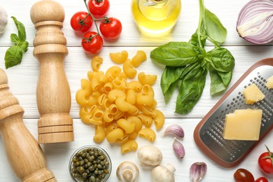 Photo of Pile of pasta, grater, shakers and products on white wooden table, flat lay