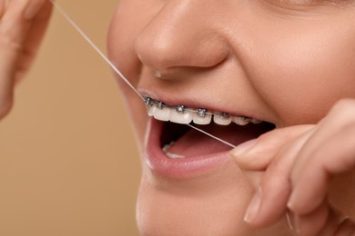 Woman with braces cleaning teeth using dental floss on brown background, closeup