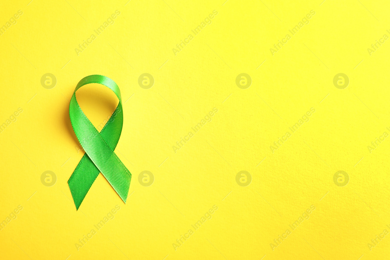 Photo of Green ribbon on color background, top view. Cancer awareness