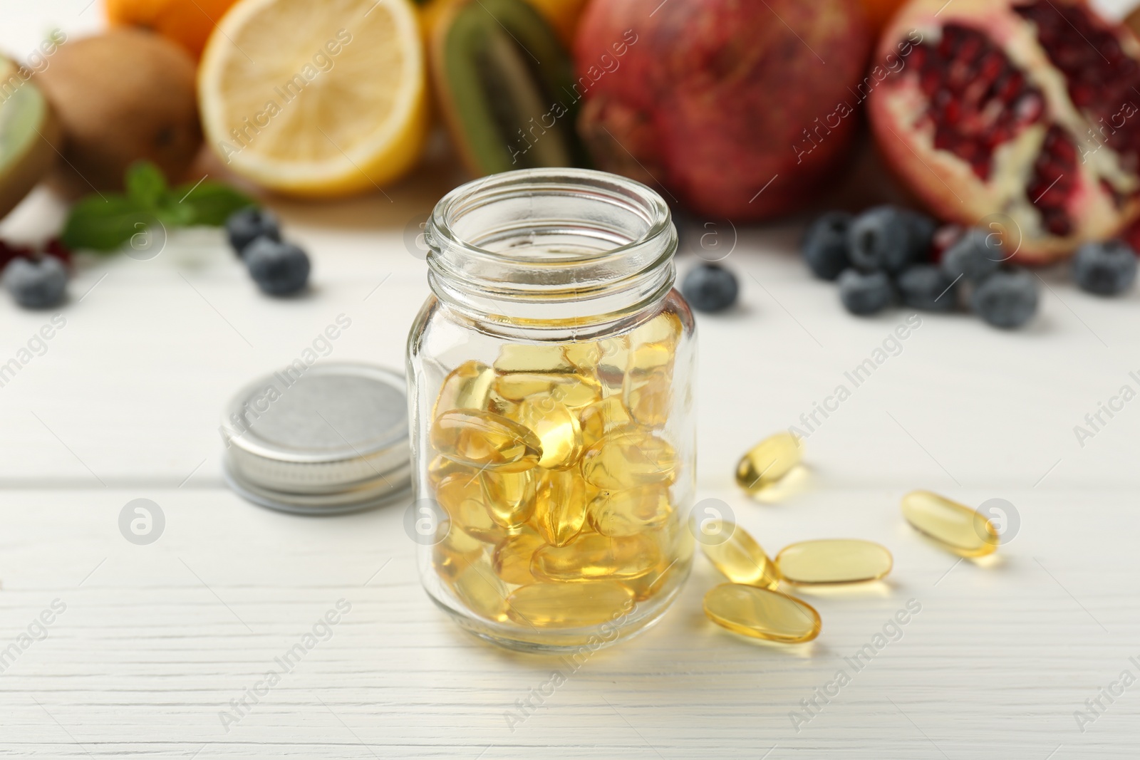 Photo of Vitamin pills in bottle and fresh fruits on white wooden table