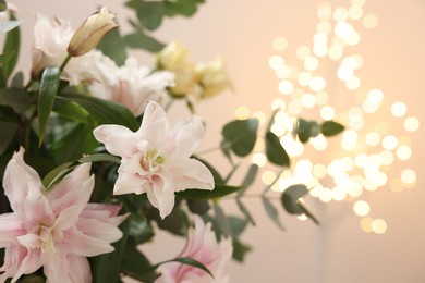 Photo of Bouquet of beautiful lily flowers against beige background with blurred lights, closeup. Space for text