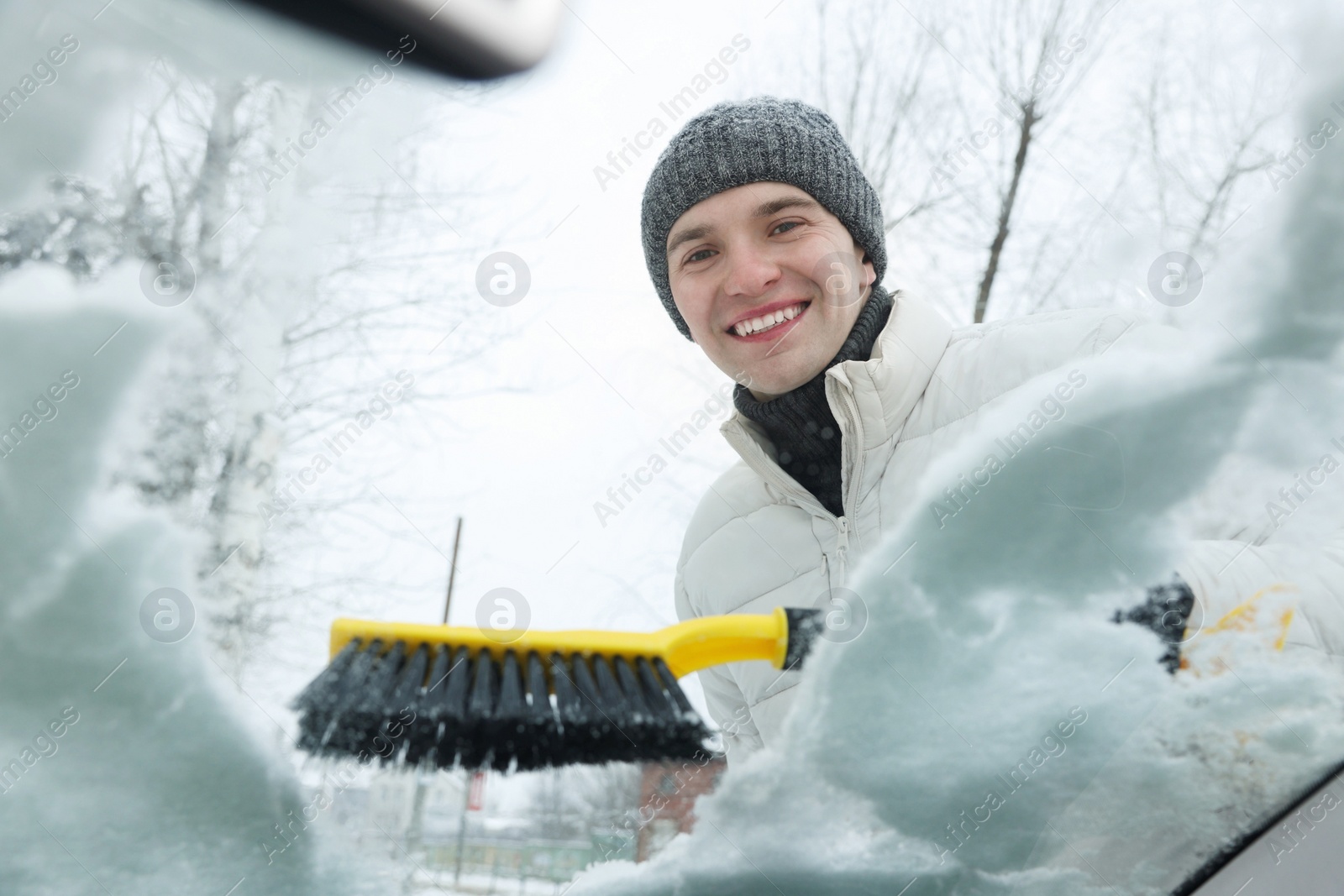 Photo of Man cleaning snow from car windshield, view from inside