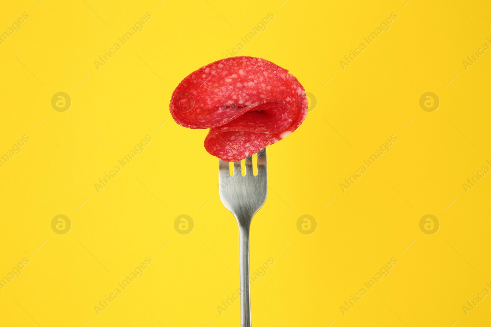 Photo of Fork with tasty slice of salami on yellow background