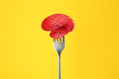Fork with tasty slice of salami on yellow background
