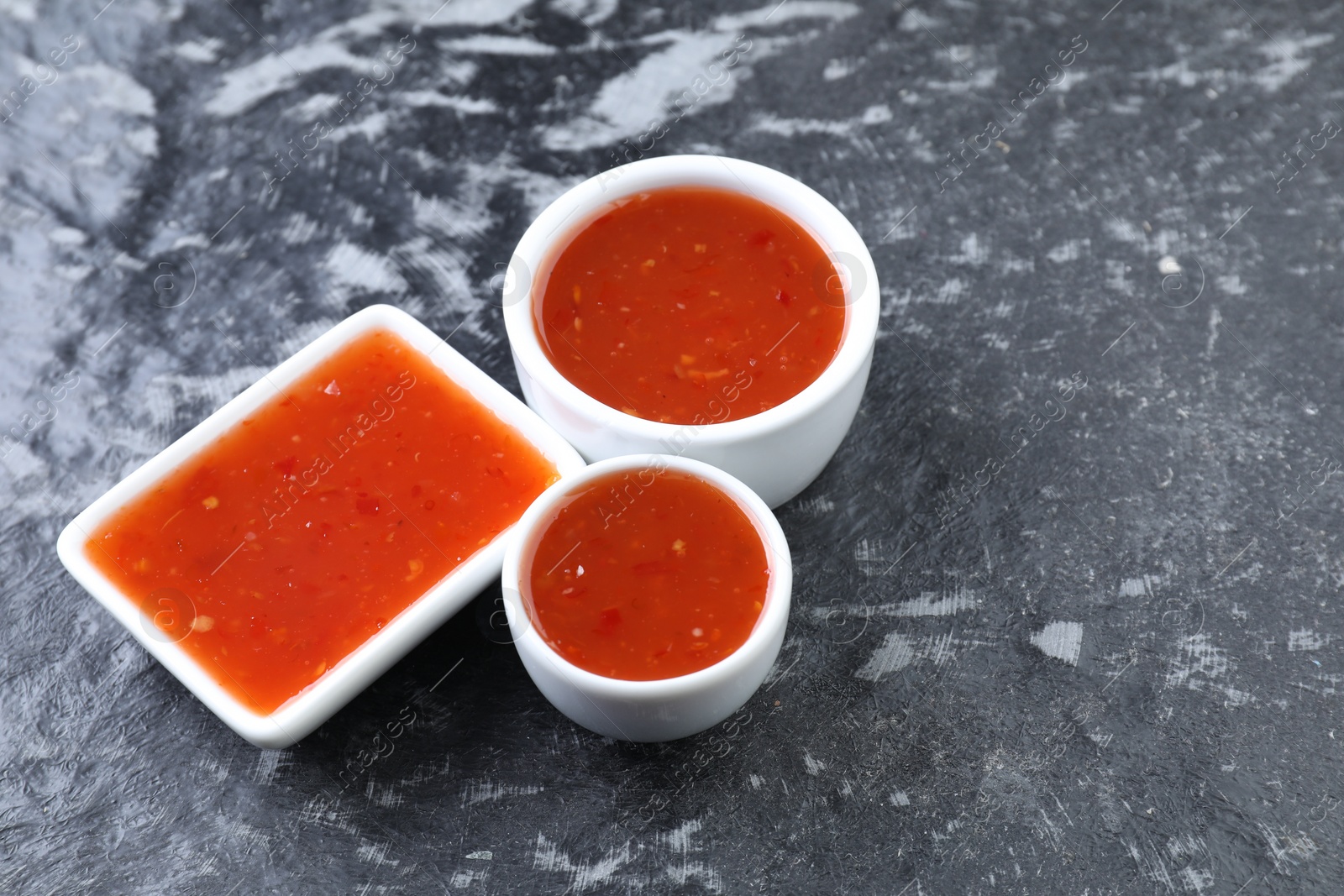 Photo of Spicy chili sauce on black textured table, space for text