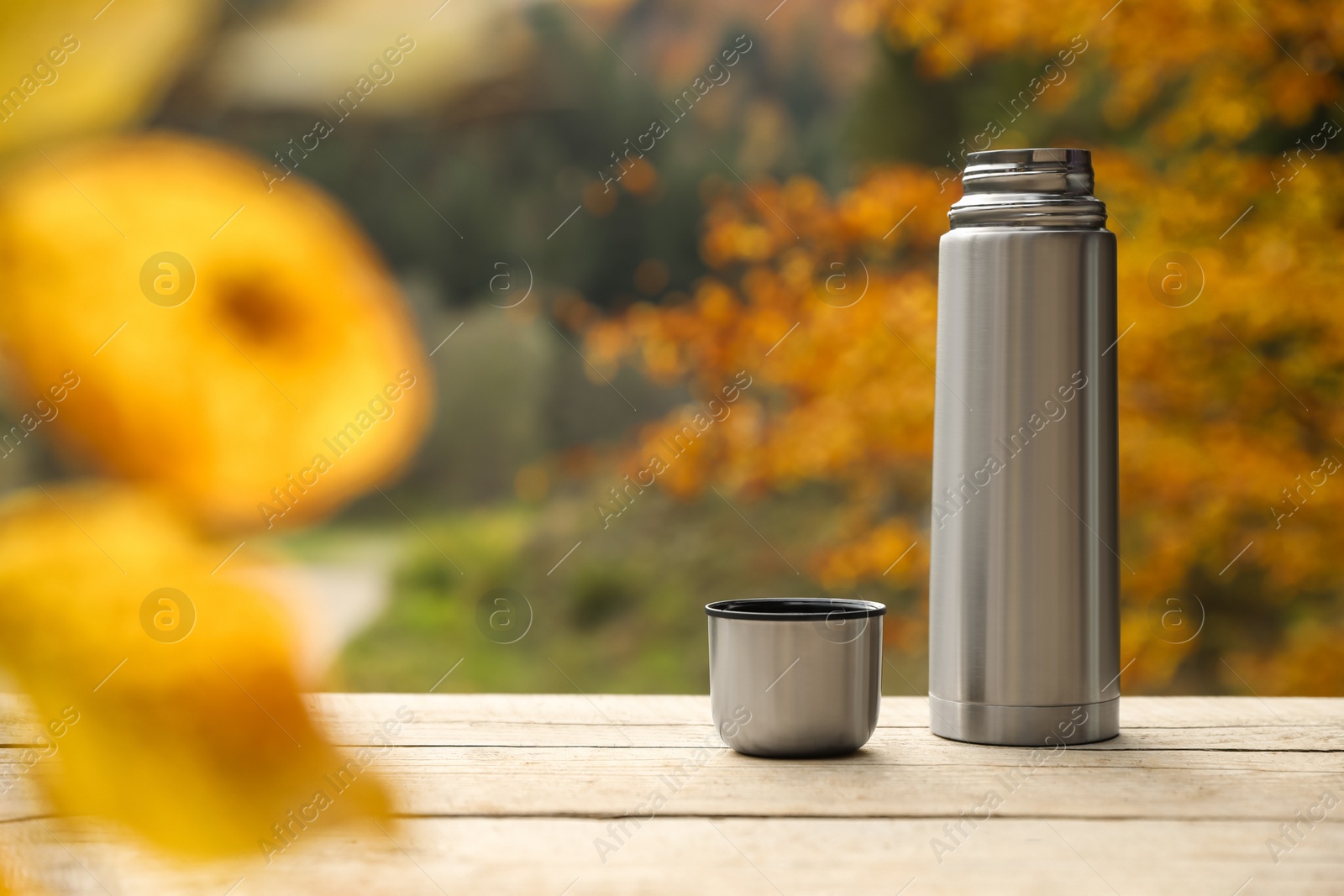 Photo of Metallic thermos and cup lid on wooden table outdoors, space for text