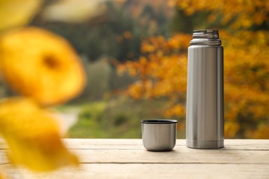 Photo of Metallic thermos and cup lid on wooden table outdoors, space for text