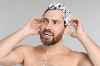 Happy man washing his hair with shampoo on grey background