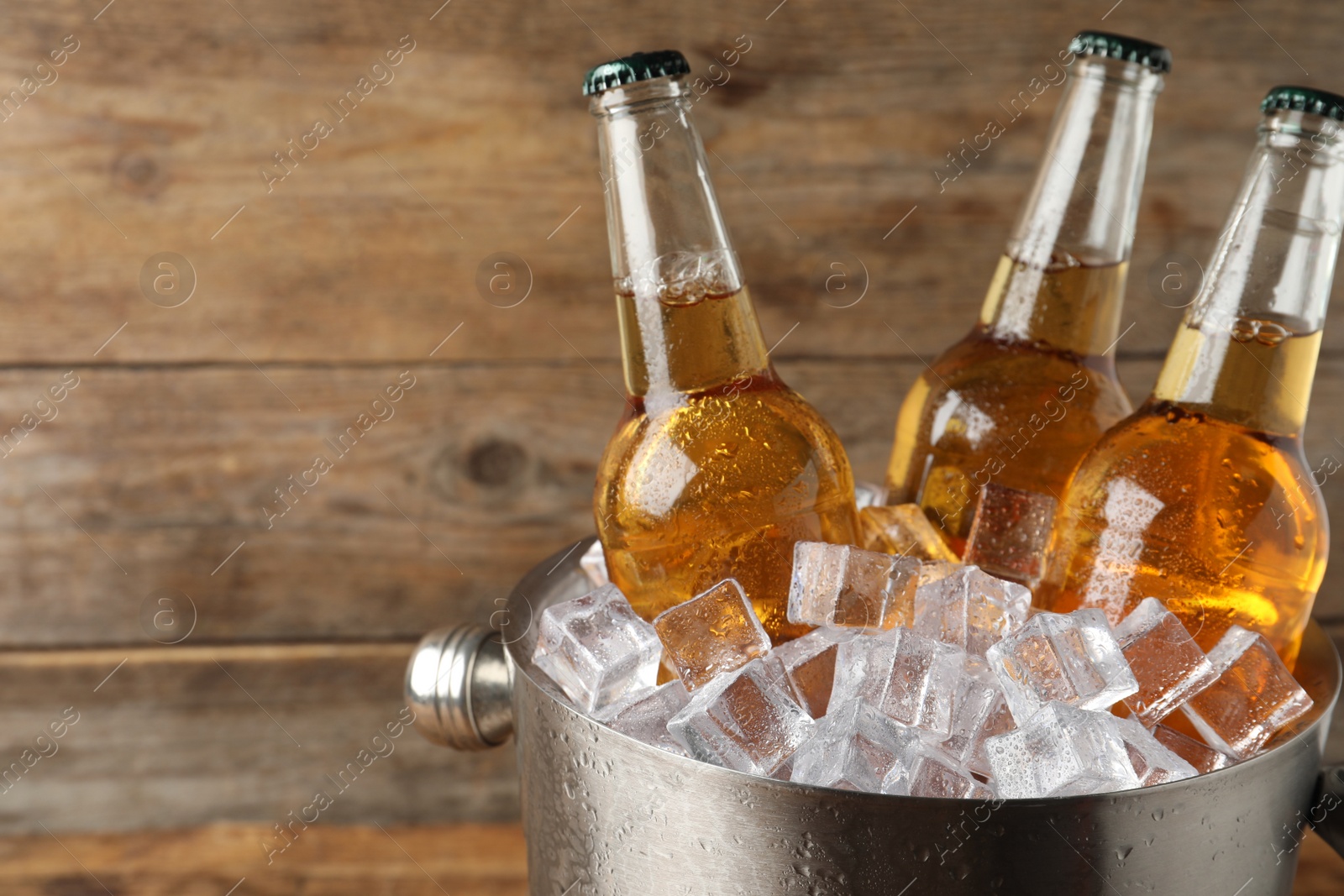 Photo of Metal bucket with beer and ice cubes on wooden background. Space for text