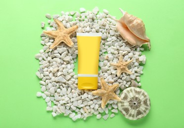 Photo of Suntan cream tube, seashells and white marble pebbles on light green background, flat lay