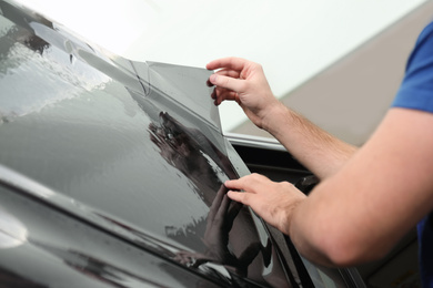 Worker tinting car window with foil in workshop, closeup