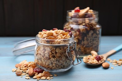 Photo of Jars of tasty granola with nuts and dry fruits on light blue wooden table