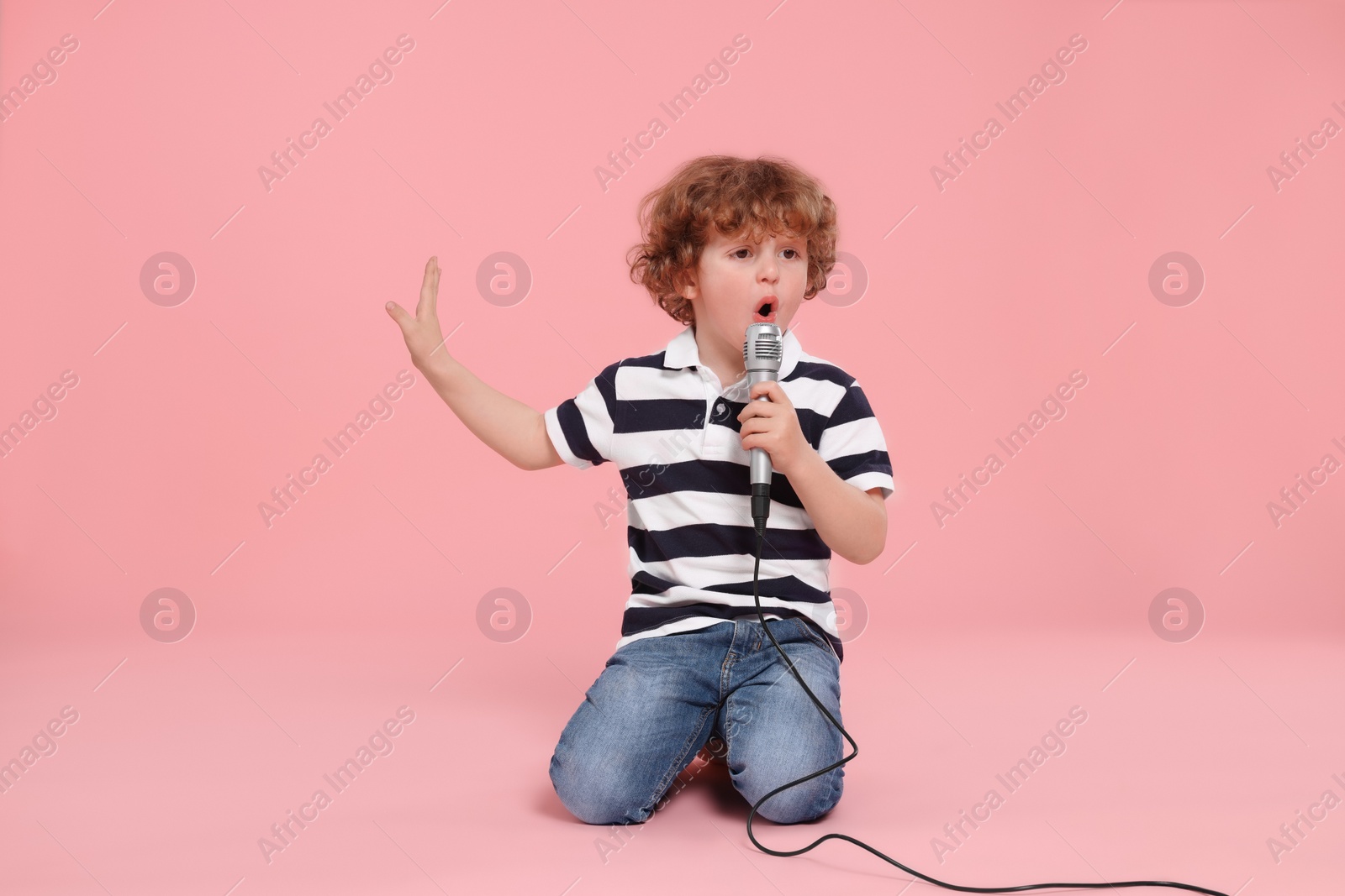 Photo of Cute little boy with microphone singing on pink background