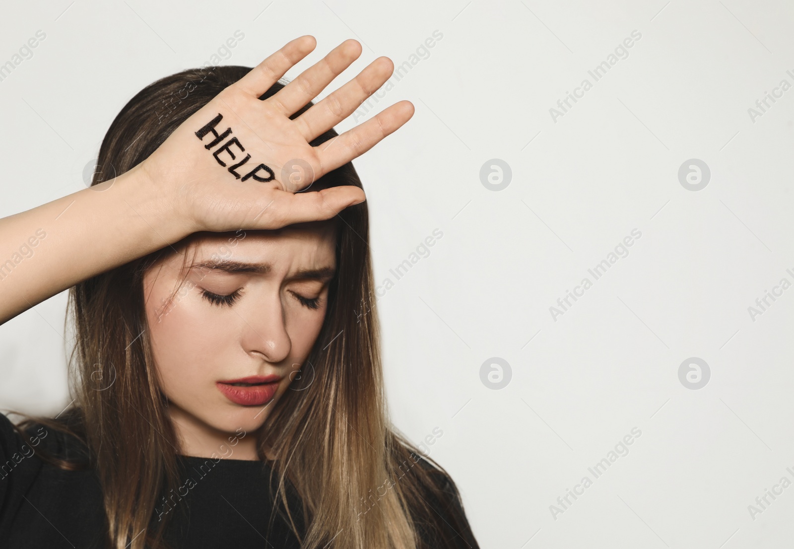 Photo of Young woman with word HELP written on her palm against light background. Space for text