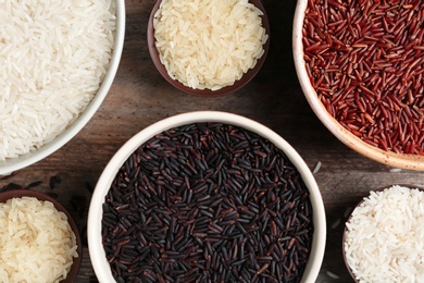 Flat lay composition with brown and other types of rice in bowls on wooden background