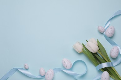 Many painted Easter eggs, tulip flowers and ribbon on light blue background, flat lay. Space for text