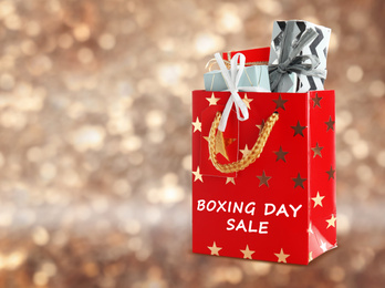 Image of Red shopping bag with text Boxing Day Sale full of gifts on blurred gold background, closeup. Space for text