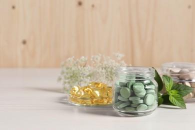 Photo of Jars with different pills and mint on white wooden table, space for text. Dietary supplements